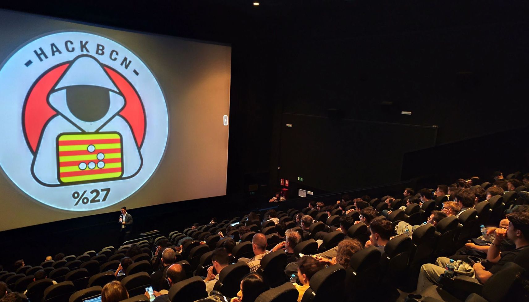 MetaDefender Sandbox Team presents groundbreaking research at HackBCN, showing a speaker and audience in a dark auditorium