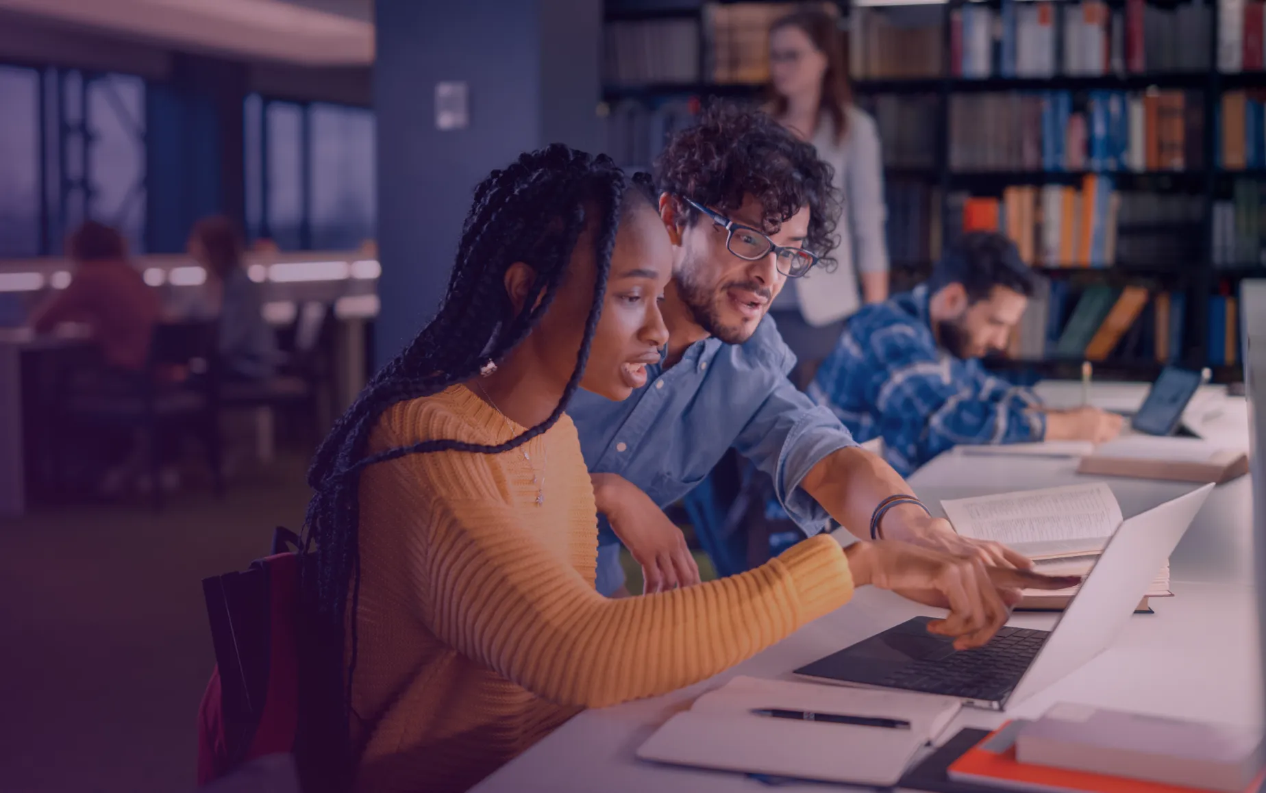 Dois estudantes a colaborar num trabalho de curso sobre cibersegurança num ambiente de estudo de biblioteca