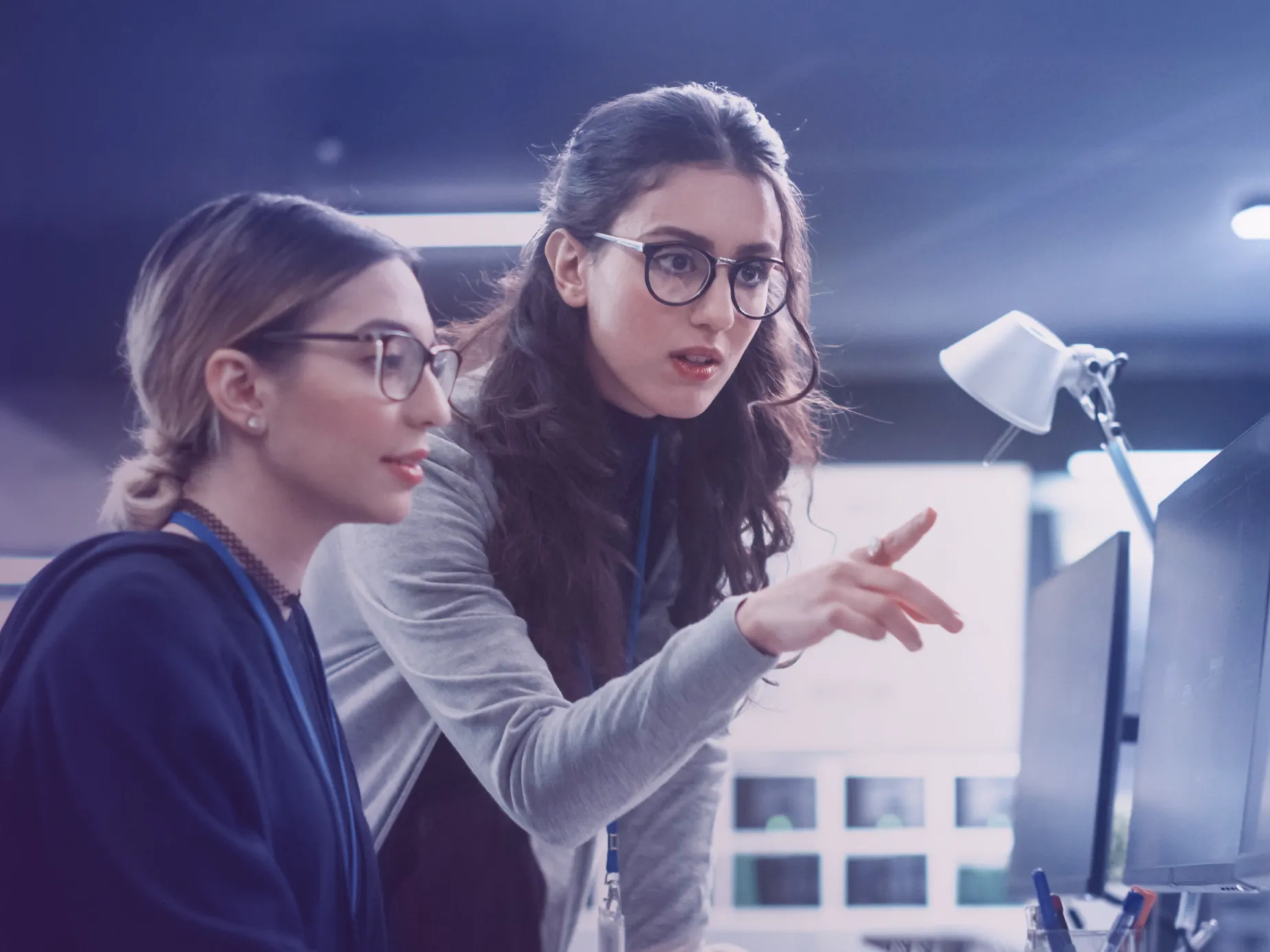 Two women at computers discussing cybersecurity training in an office setting