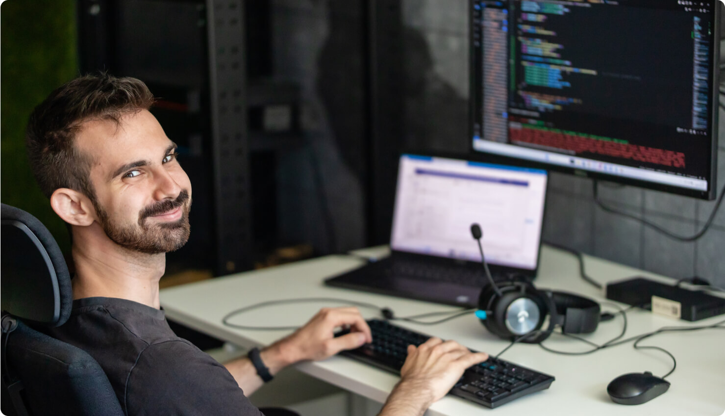 adrian sitting in front of a laptop, computer monitor, and keyboard and smiling