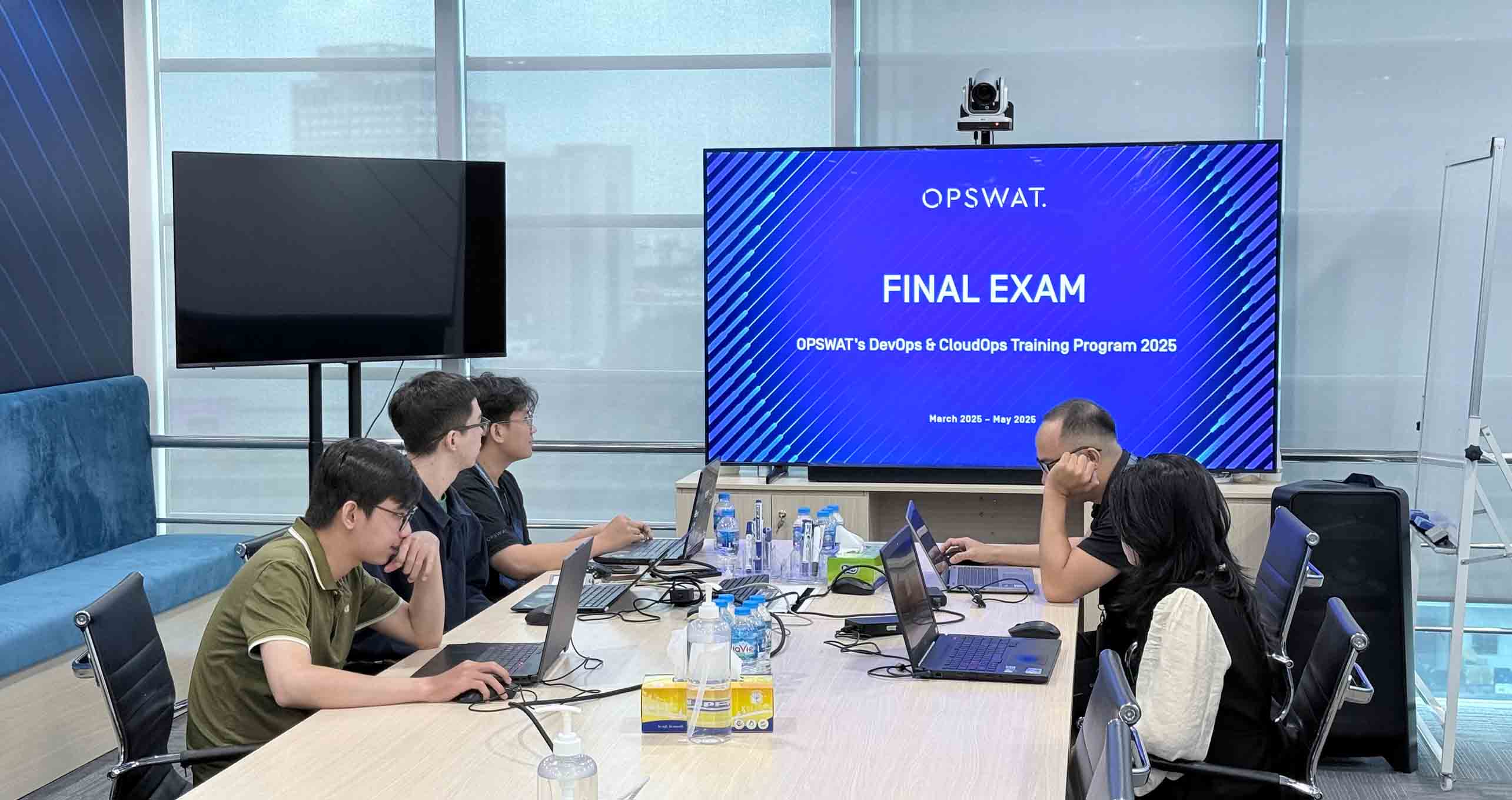 Interns collaborate at a table with laptops during OPSWAT DevOps and CloudOps Internship Experience in Cybersecurity 2025