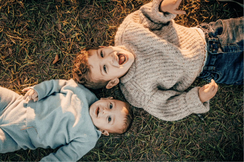 overhead shot of Carlo's two young children lying on grass, laughing and looking up at the camera