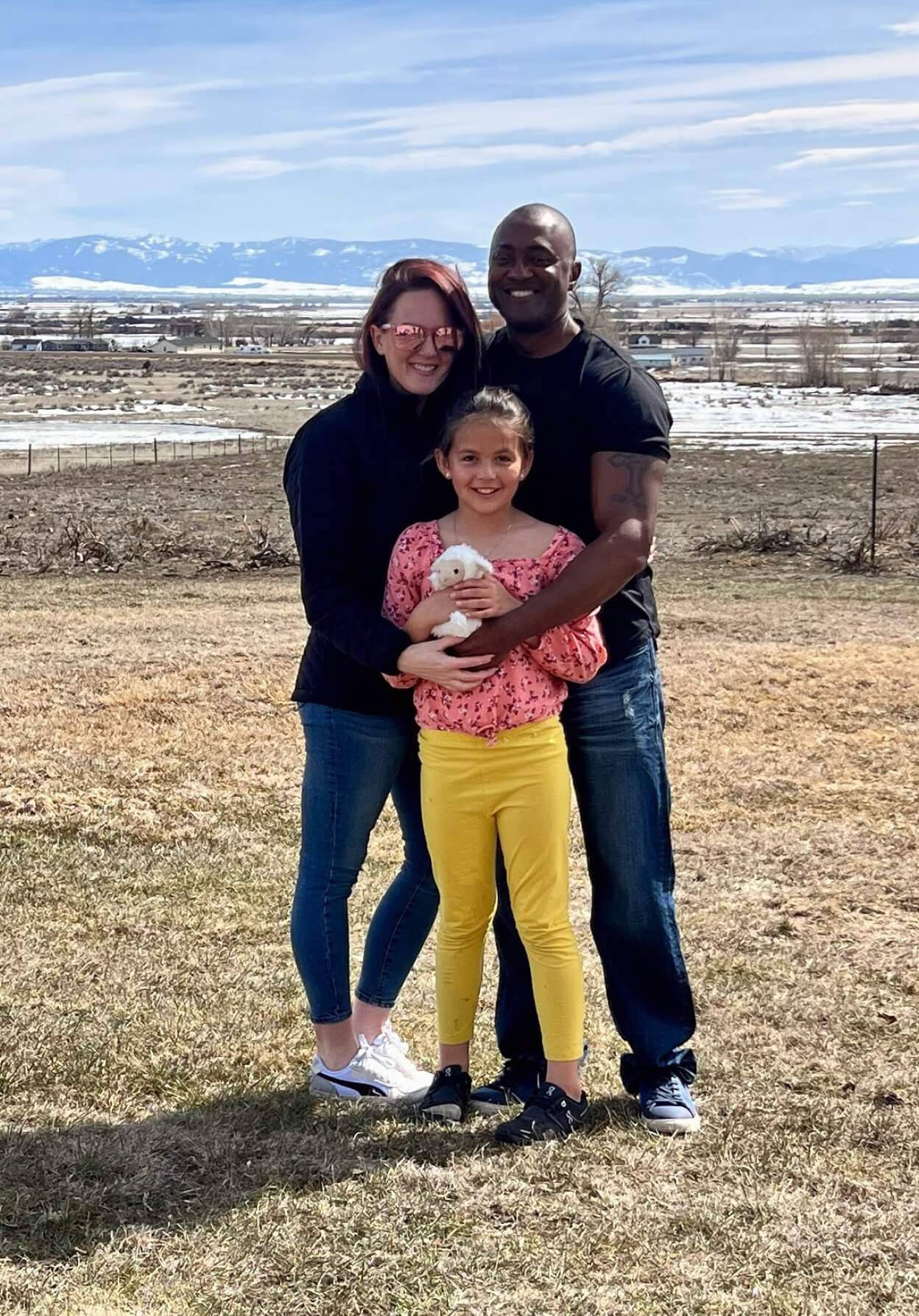 Laci Glenn and family standing in a field with mountains in the background