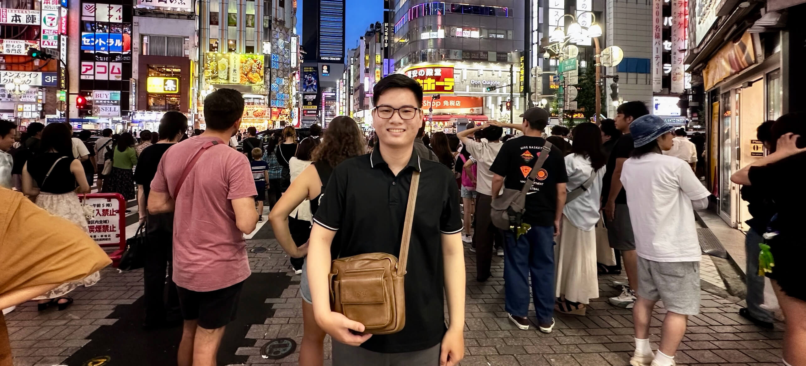 ネオンと雑踏でにぎわう都会の夜景の中で、カメラに向かって微笑むソン・タイ。