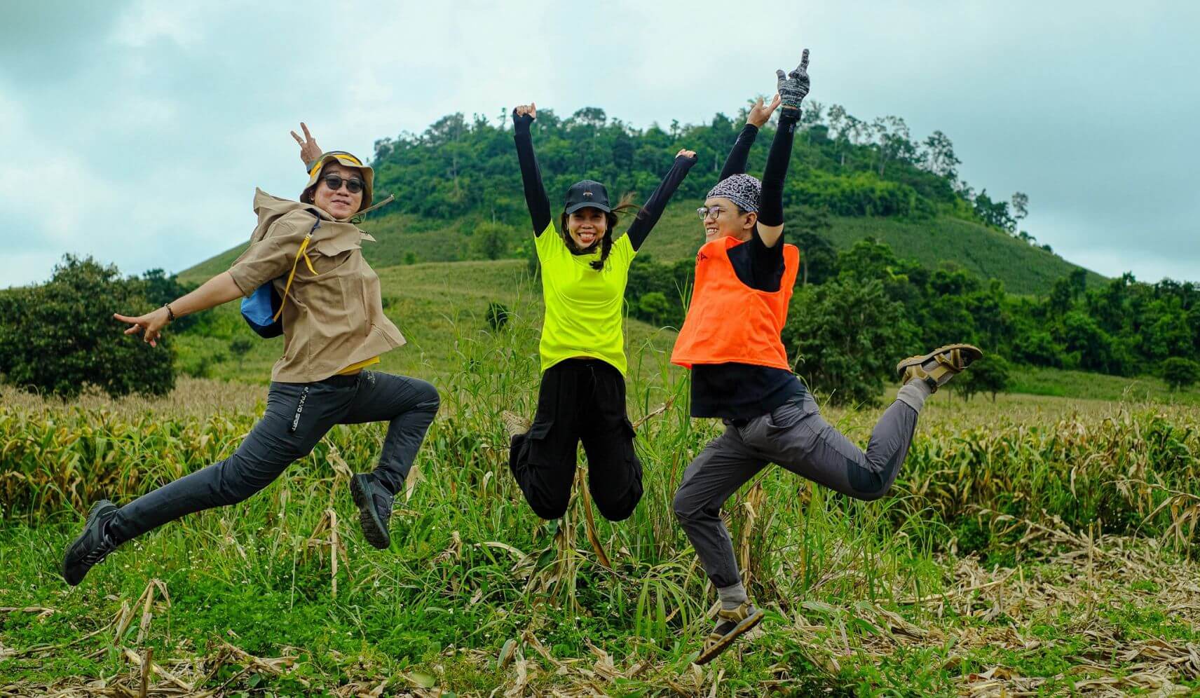 three people jumping in the air in front of a green hill