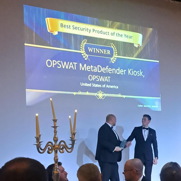cerimónia de entrega do prémio "Melhor Produto de Segurança do Ano" a OPSWAT MetaDefender  Kiosk , com os dois homens a apertarem as mãos no palco