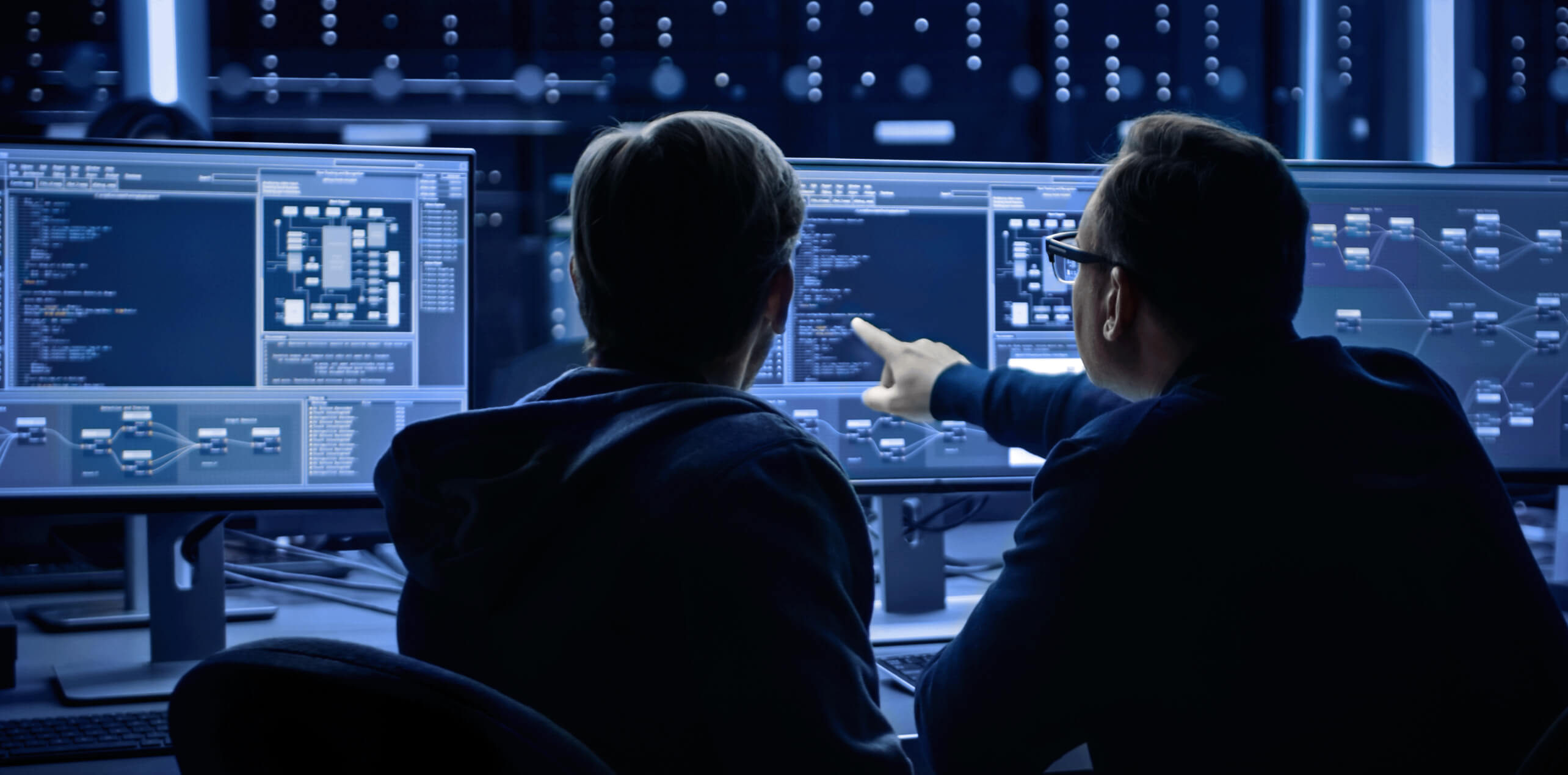 两名网络安全专业人员在网络运营中心分析多个屏幕上的数据,讨论 OT 安全策略