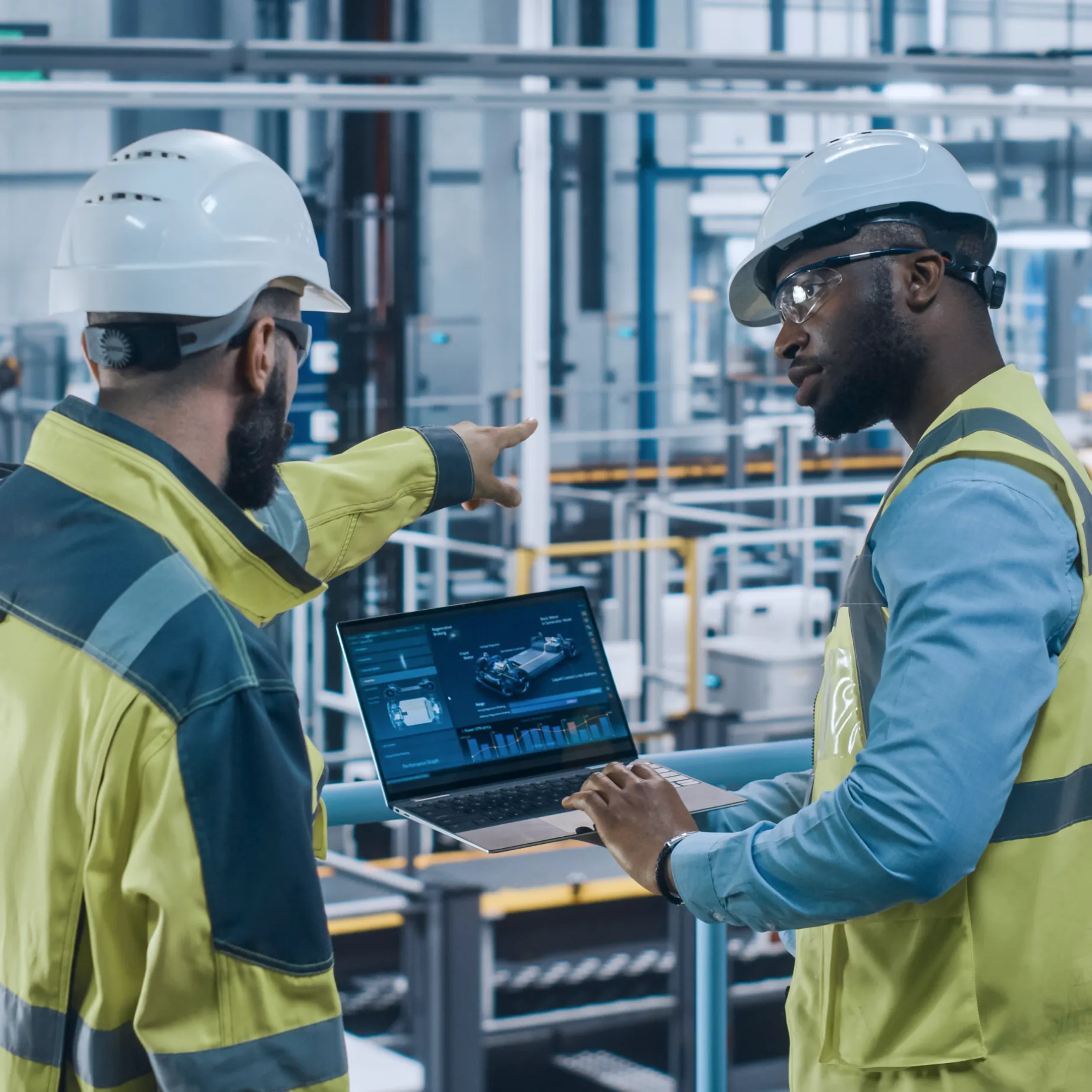 Engineers in a factory using a laptop to monitor manufacturing cybersecurity solutions in real-world deployments