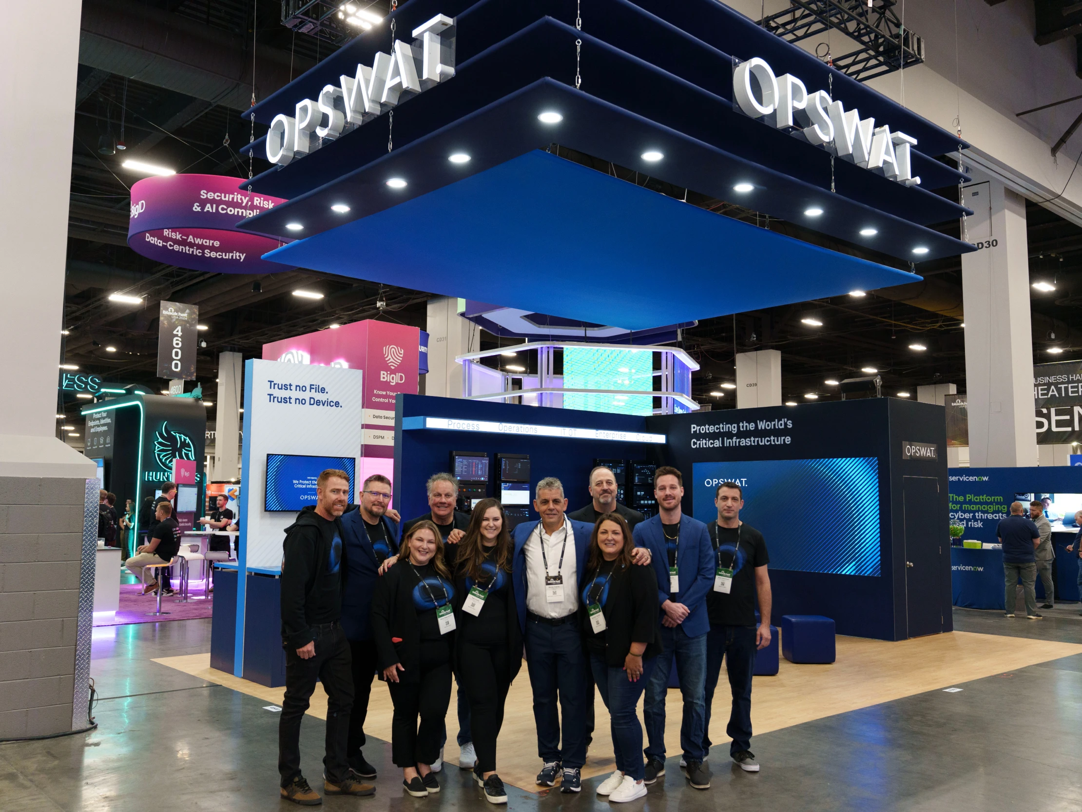 Gruppo allo stand OPSWAT sul palco del Black Hat 2025 con display di cybersecurity sullo sfondo
