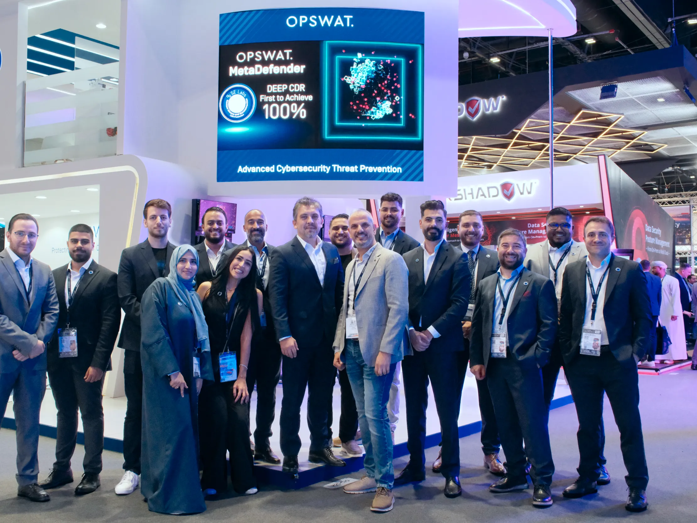 Group of OPSWAT professionals smiling in front of a screen promoting OPSWAT's MetaDefender, Advanced Cybersecurity Threat Prevention solution