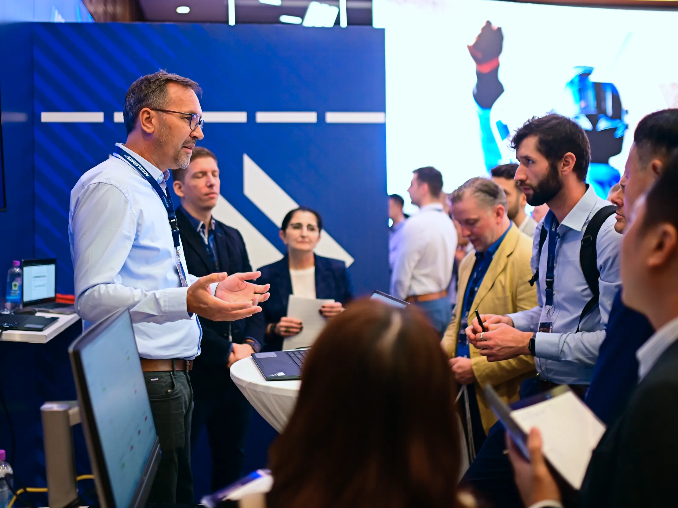 People networking and discussing within a group gathered around a presenter in a tech event setting